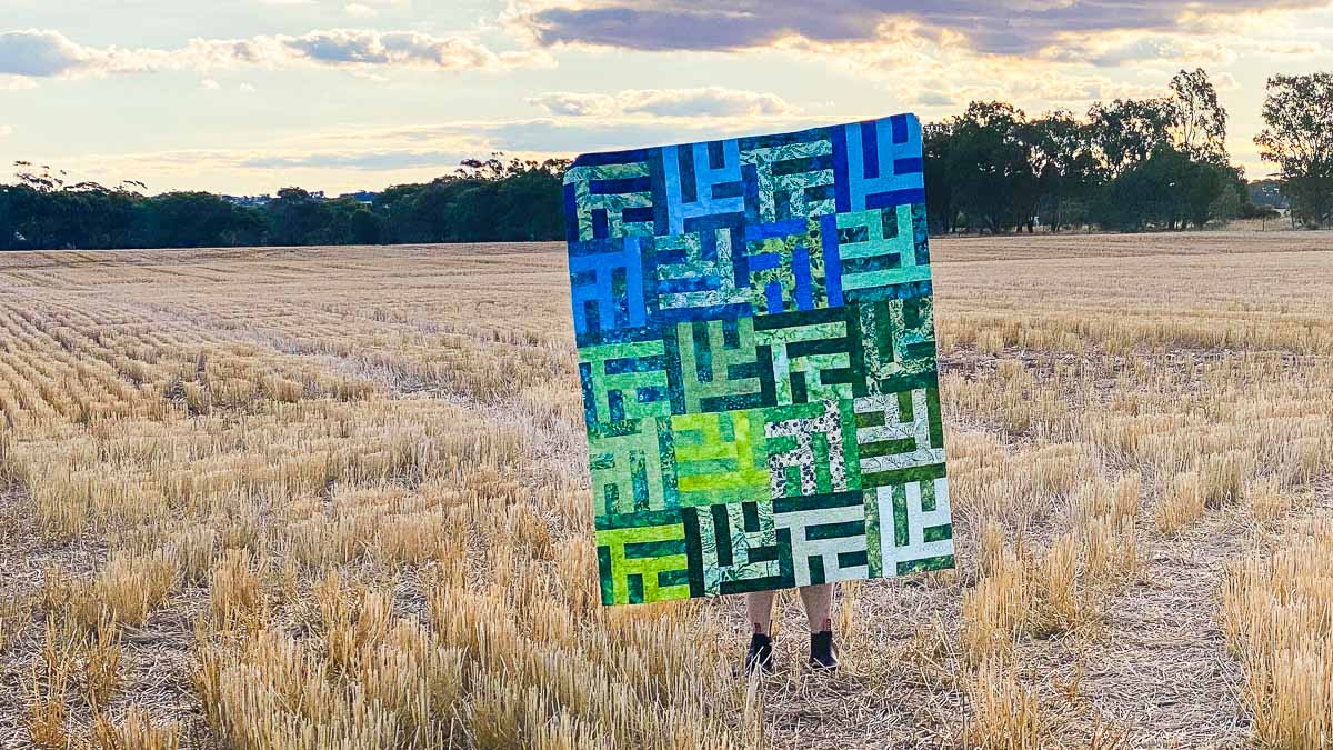 A quilt with a modern maze-like design in shades of green and blue.